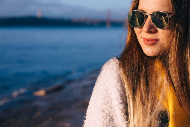молодая девушка в солнечных очках с красными губами позирует на фоне набережной. - Фото, изображение