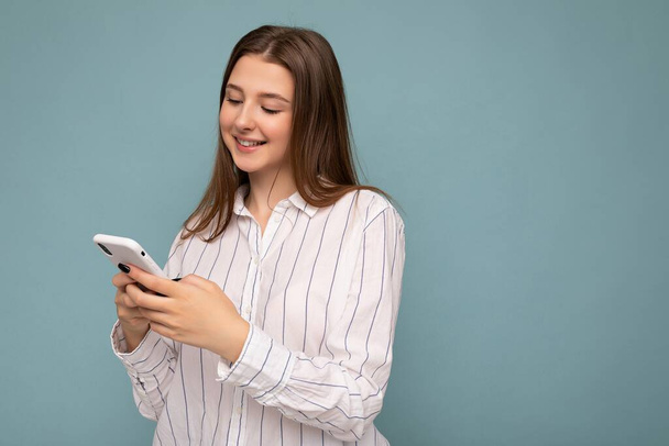 Mooie jonge vrouw dragen casual kleding geïsoleerd over achtergrond surfen op het internet via telefoon kijken naar mobiele scherm - Foto, afbeelding