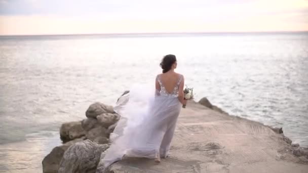 Egy menyasszony esküvői csokorral sétál a mólón, szoknyája repked a szélben. - Felvétel, videó