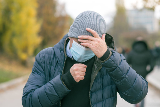Onjuiste manier van niezen of hoesten in een beschermend medisch gezichtsmasker, buiten. Voorkomen van de verspreiding van de ziekte van Coronavirus 2019 (COVID-19)) - Foto, afbeelding
