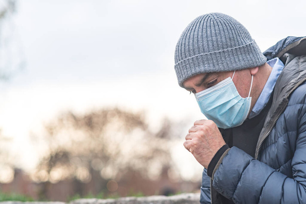 Incorrect way of sneezing or coughing into a protective medical face mask, outdoors. Prevent the spread of the Coronavirus Disease 2019 (COVID-19) - Photo, Image