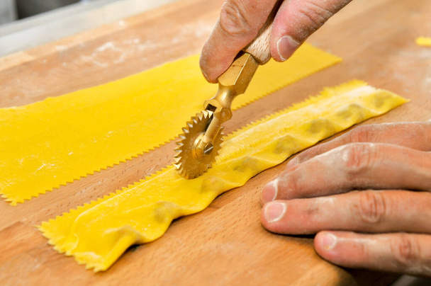 Ravioli del plin, typical pasta of Langhe, Piedmont, Italy - hand cutting with rotary knife of agnolotti on wooden cutting board - Photo, Image