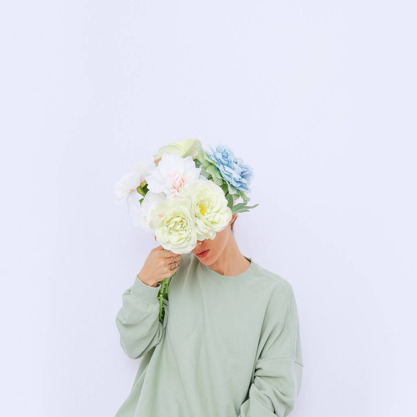 Yüzünün önünde çiçekleri tutan bir kız şık, sıradan bir çevre görüntüsüyle. Bahar koleksiyonu. Minimalist - Fotoğraf, Görsel