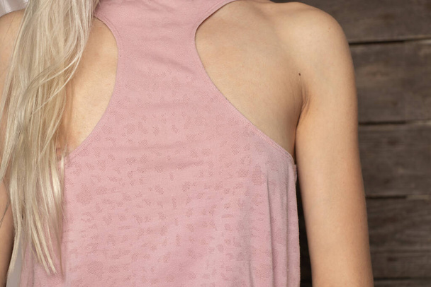 Το στήθος του κοριτσιού είναι καλυμμένο με ένα ροζ ανοιχτό μπλουζάκι, το στήθος ενός νεαρού κοριτσιού με ένα μπλουζάκι. - Φωτογραφία, εικόνα