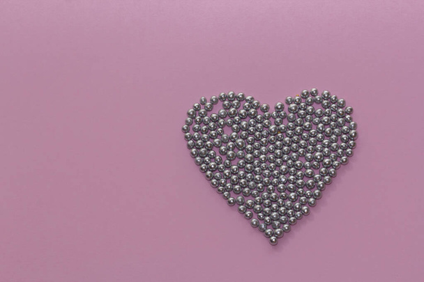 salpicaduras de perlas plateadas dispuestas en forma de corazón sobre un fondo rústico rosado. Día de San Valentín, tarjeta de felicitación. Aspersores para pastelería y pastelería, Espacio para copias, vista superior - Foto, imagen
