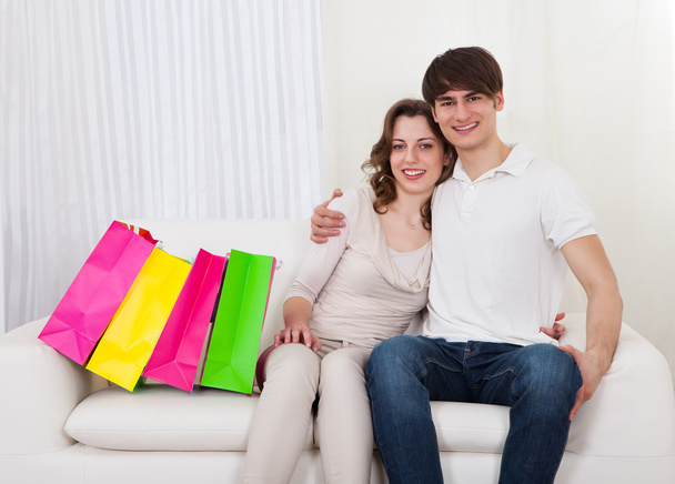 Happy couple sitting on couch with shopping bags - Foto, imagen