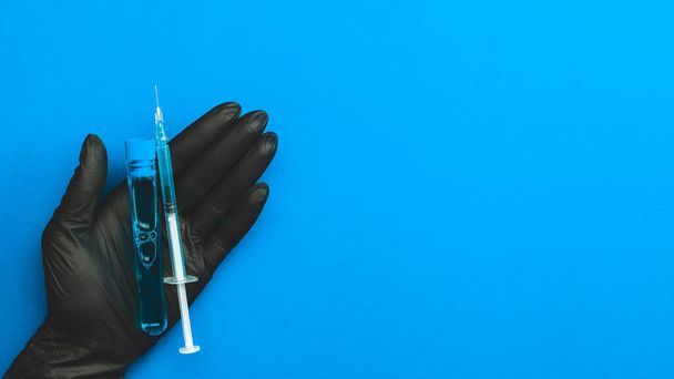 Aşı şişesi. Eldivenli doktor grip virüsünü ve koronavirüsü korumak için şırıngayı elinde tutuyor. Aşı mavi renkte izole edildi. Şırınga, tıbbi enjeksiyon - Fotoğraf, Görsel