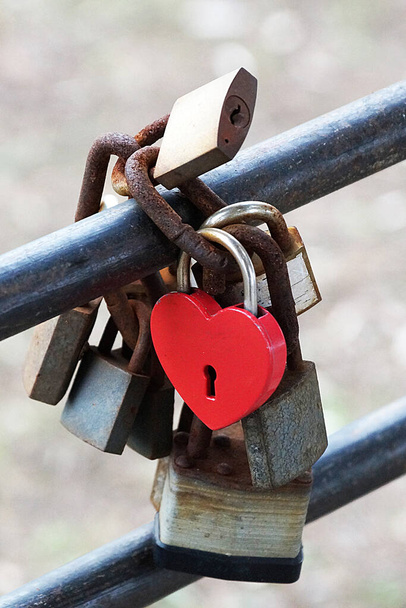 un candado rojo en forma de corazón como símbolo del amor eterno cuelga de la barandilla con otras cerraduras. - Foto, Imagen