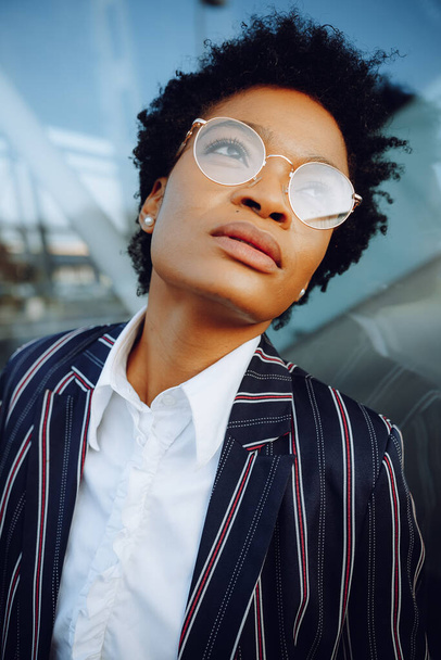 4k. Charming African American woman in modern striped suit and looking to nowhere. Businesswoman or student. Close up. Portrait. - Photo, image
