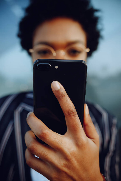4k. Charmante Afroamerikanerin hält ihr Handy in die Kamera. Unternehmerin oder Studentin. Nahaufnahme. - Foto, Bild