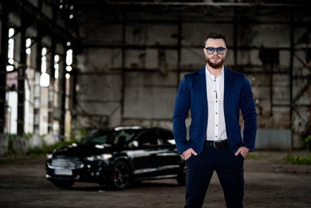 Elegant young handsome man. Fashion portrait of businessman on abandoned warehouse background. Fashion car on the background. - Foto, afbeelding