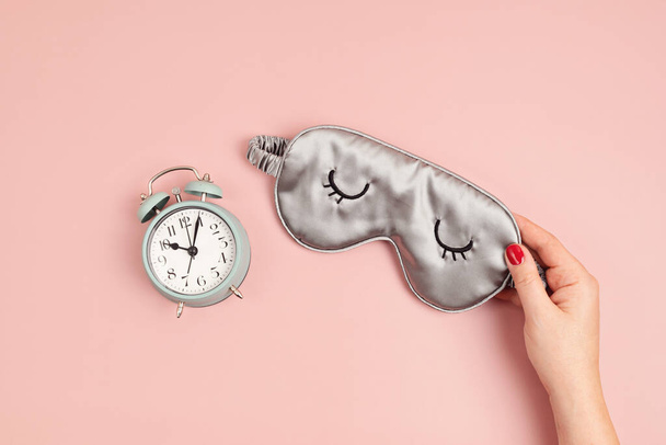 Sleeping mask and classic alarm clock on pink pastel background.  Minimal concept of rest, quality of sleep, good night, insomnia, relaxation. Flat lay, top view mock up - Photo, Image