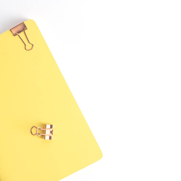 A yellow notepad and two copper paper clips lie on a white background, top view. Stationery and minimalism - 写真・画像