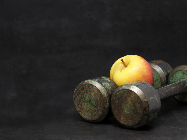 Старі залізні гантелі та яблуко, спорт та дієта. Темний фон
. - Фото, зображення