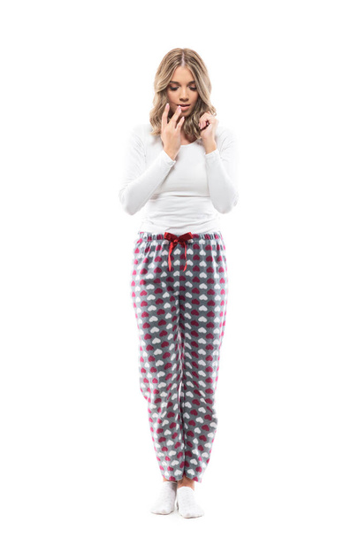 Jonge mooie vrouw in comfortabele pyjama die lippen aanraakt die naar beneden kijken. Huiselijk leven. Volledige lichaamslengte geïsoleerd op witte achtergrond.  - Foto, afbeelding