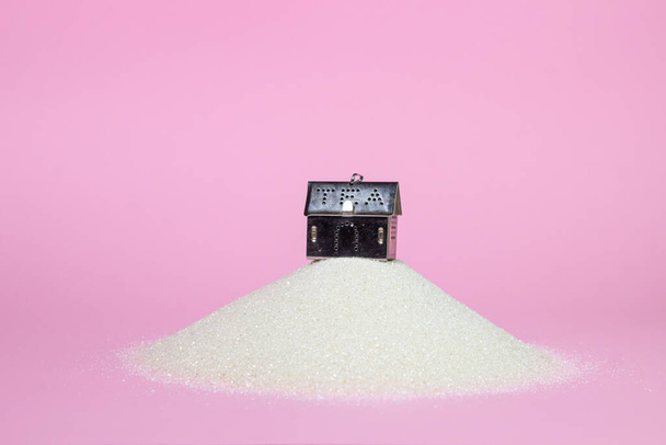 Στραγγιστήρι τσαγιού σε σχήμα σπιτιού σε ροζ φόντο. Ένα σουρωτήρι για τσάι πάνω σε ένα σωρό ζάχαρη. Ωραία ιστορία. Σπίτι στο λόφο - Φωτογραφία, εικόνα
