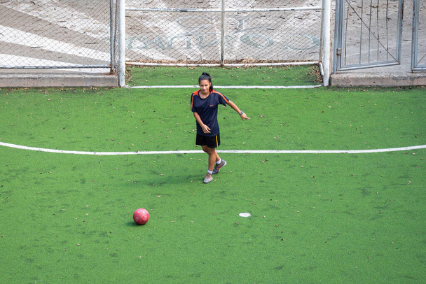 Medellin, Antioquia, Colombia - December 23 2020: Μια νεαρή Ισπανίδα γυναίκα σε Black Sportswear Practices και παίζει ποδόσφαιρο σε δημόσιο γήπεδο με πράσινο συνθετικό χόρτο πεδίο - Φωτογραφία, εικόνα