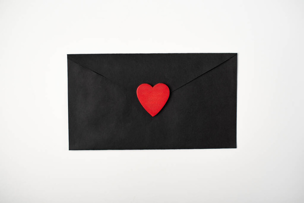 Black envelope with the red heart on the white background. Flat lay, top view. Romantic love letter for Valentine's day concept. - Zdjęcie, obraz