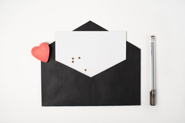 Black envelope with a blank sheet of paper inside and red heart on the white background. Romantic love letter for the Valentine's day concept. Space for text. - Valokuva, kuva