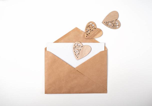 Craft envelope with a blank sheet of paper inside and wooden hearts on the white background. Romantic love letter for the Valentine's day concept. Space for text. - Foto, immagini