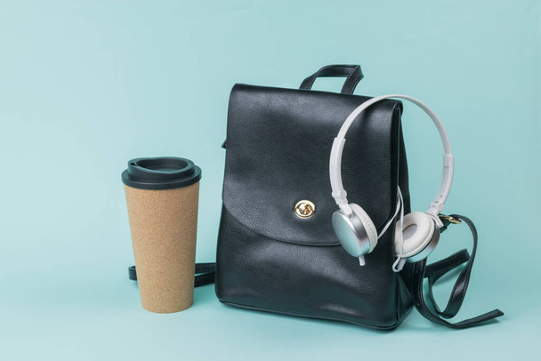 Δερμάτινη τσάντα πλάτης, φλιτζάνι καφέ και λευκά ακουστικά σε μπλε φόντο. Τρόπος ζωής. - Φωτογραφία, εικόνα