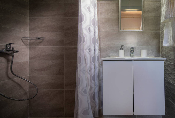 Nahaufnahme eines kleinen Badezimmers mit Dusche und weißem Waschbecken. Vorderseite des Toilettenraums im modischen Stil graue Keramikfliese - Foto, Bild