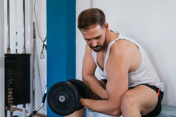 Egy férfi bicepszet csinál egy súlyzóval. Fitness tornaterem, sport és egészséges életmód koncepció - Fotó, kép