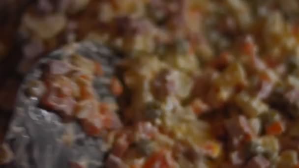 Zubereitung des traditionellen russischen Salats Olivier. Mischen Sie die Zutaten in einer Glasschüssel - grüne Erbsen, Kartoffeln, Wurst, Karotten, Eier, Mayonaisse. 4K-Video. Ansicht von oben, Makro - Filmmaterial, Video