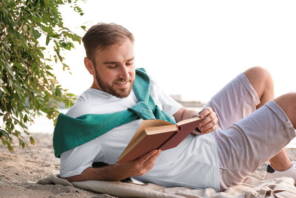 Молодий чоловік читає книгу на піщаному пляжі біля моря
 - Фото, зображення
