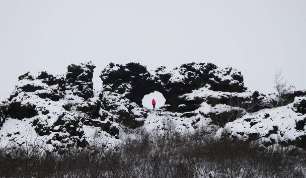 Turisti henkilö punainen takki seisoo reikä ikkuna Dimmuborgir tulivuoren laava kentät rock muodostumista Myvatn Islanti - Valokuva, kuva