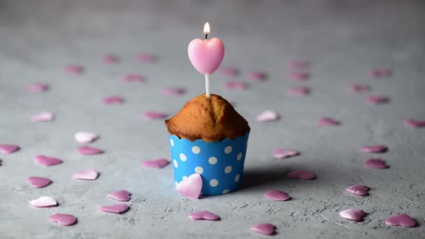 4k Valentijnsdag cupcake of muffin met roze hart vorm kaars in blauwe decoratie vorm op een grijze achtergrond met kleine roze harten, Viering Valentijnsdag. Vakantie, huwelijksverjaardag, verjaardag - Video