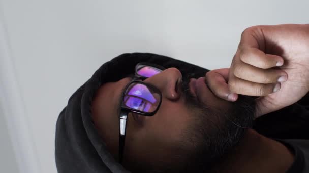 Homme de minorité ethnique à capuchon avec des écrans d'ordinateur reflétés dans les lunettes. Vidéo verticale, verrouillée - Séquence, vidéo
