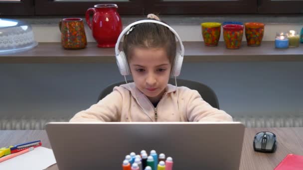 Dizüstü bilgisayarla çalışan küçük bir kız. Bilgisayarla öğrenen üzgün kız öğrenci. Sıkıcı çocuk okul ödevi yapıyor ve koronavirüs salgını sırasında e-öğreniyor. Evde uzaktan eğitim - Video, Çekim