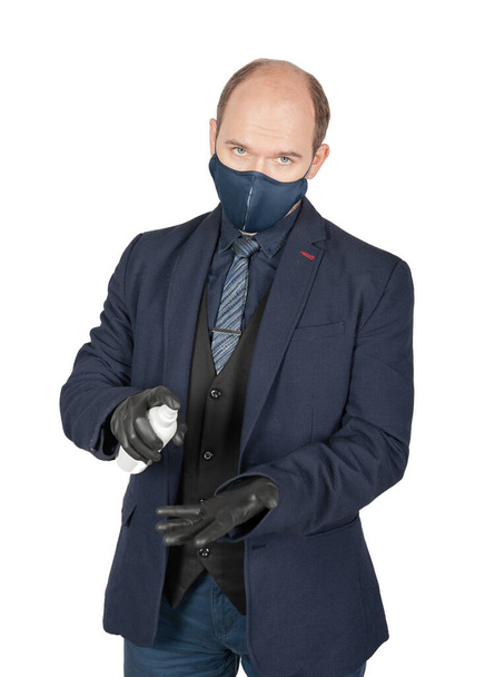 Beau jeune homme d'affaires avec masque de protection contre le virus médical chirurgical et gants noirs tenant une bouteille antiseptique isolée sur du blanc - Photo, image