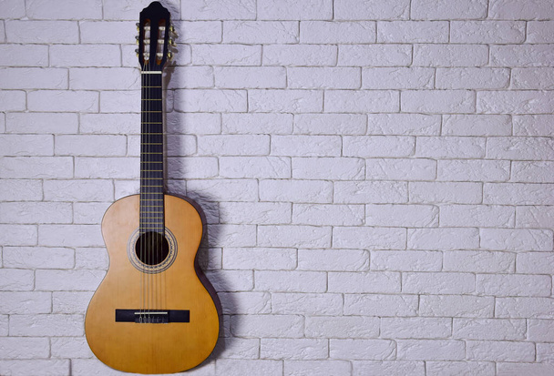Eine Akustikgitarre steht aufrecht gegen eine helle Ziegelwand auf der linken Seite. Viel Platz rechts für Bildunterschrift oder Text - Foto, Bild