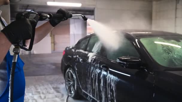 Araba yıkama ve temizlik. Profesyonel bir işçi araba yıkama makinesinde siyah bir arabayı yıkıyor.. - Video, Çekim