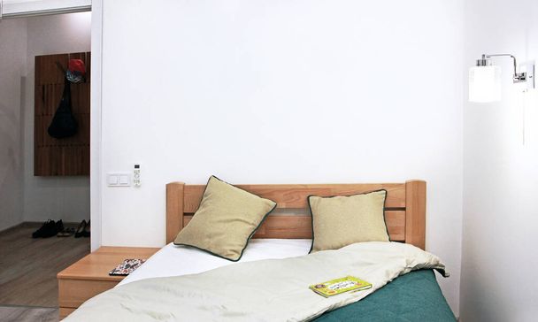 уютный панельный интерьер с зеленым покрывалом, две подушки, светящаяся булочка, книга на покрывале с дверью в коридор - Фото, изображение