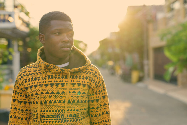 Giovane nero africano uomo pensando mentre guardando al lato e indossando felpa con cappuccio all'aperto - Foto, immagini