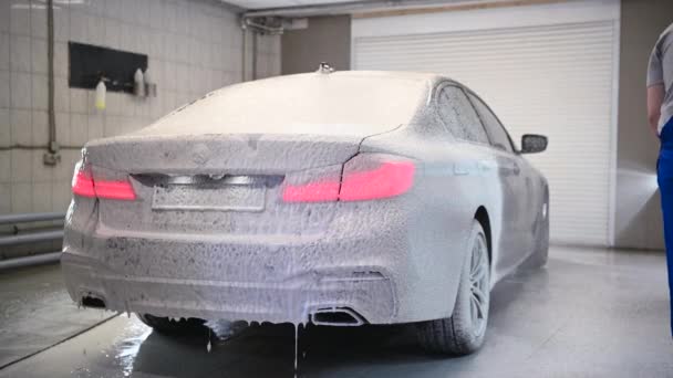 Männliche Autoexperten decken dunkle Luxusautos beim Waschservice mit Schaum ab. Mechaniker, der alle Vorbereitungen für eine ordnungsgemäße Reinigung des modernen Fahrzeugs trifft. - Filmmaterial, Video