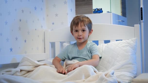 Retrato de un lindo niño jugando con juguetes en la cama antes de irse a dormir por la noche. CHild jugando con juguetes y divirtiéndose - Metraje, vídeo