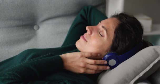 Blissful woman listens to music through modern wireless headphones - 映像、動画