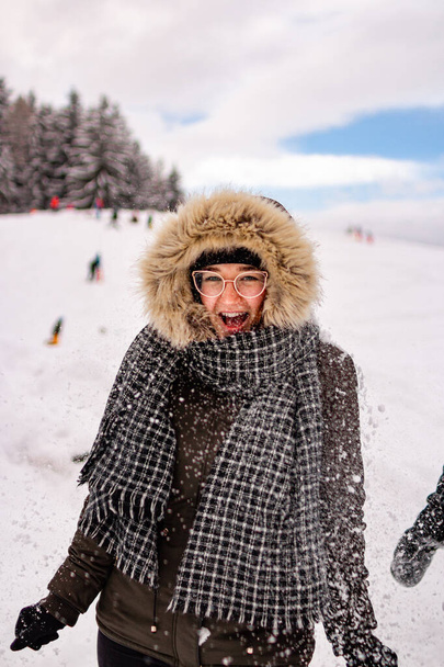 молодая женщина веселится в снегу улыбаясь, как снег брошен к ней; развлекательная активная зимняя концепция; - Фото, изображение