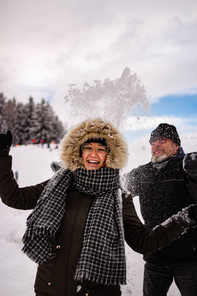 fiatal nő szórakozás a hóban mosolygós, mint a hó dobott felé apja; rekreációs aktív téli koncepció; - Fotó, kép