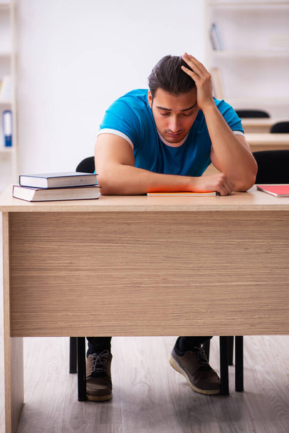 Exhausted male student preparing for the exams in the classroom - Photo, Image