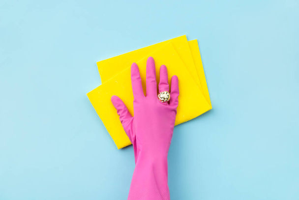 Γυναικείο χέρι σε ροζ καουτσούκ γάντι σκουπίστε από κουρέλι σε μπλε φόντο - Φωτογραφία, εικόνα