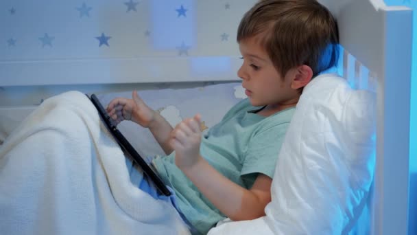 Крупним планом маленький хлопчик з планшетним комп'ютером дивиться мультфільми і грає в ігри на планшетному комп'ютері вночі перед сном
 - Кадри, відео
