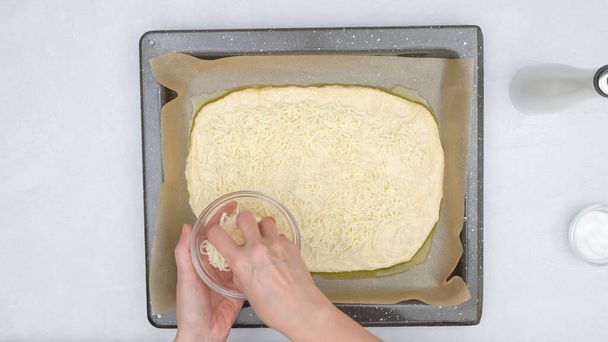 Fladenbrot mit Mozzarella-Käsebelag nach und nach Rezept. Brotteig aus nächster Nähe auf Backblech, Blick von oben - Foto, Bild