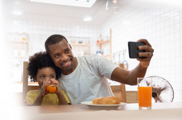 Boldog afrikai család selfie okostelefonnal otthon. Afrikai-amerikai apa és fia videohívást kezdeményez mobiltelefonnal együtt - Fotó, kép