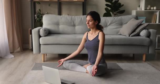 Serene woman sit cross-legged meditating listen music on laptop - Filmati, video