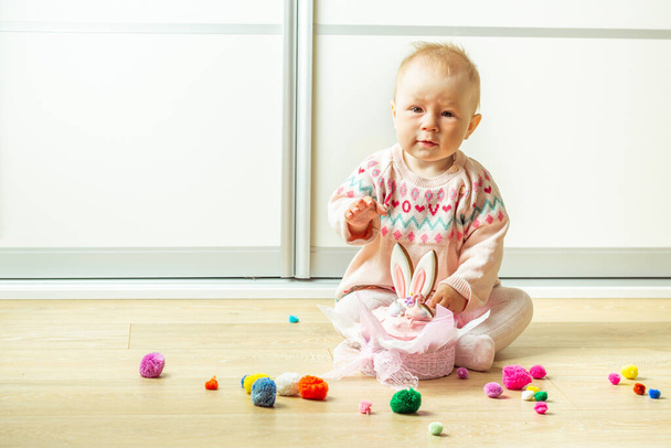 ウサギの耳のジンジャーブレッドクッキーで飾られた伝統的なイースターパンで遊んでいる小さな赤ちゃんの女の子。創造的なイースターケーキの装飾。イースター・パネトーネ。幸せな小さな子供が床で遊んでいる - 写真・画像
